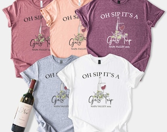 May include: Five short-sleeved t-shirts in shades of pink, peach, grey, and white. Each shirt features the text "OH SIP IT'S A Girls Trip NAPA VALLEY 2025" with a wine bottle and glass graphic. A wine bottle is visible.