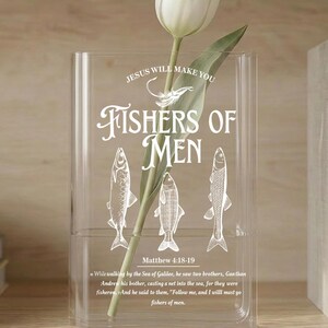 May include: A clear rectangular acrylic vase featuring white printed graphics of three fish, a fishing hook, and the text "JESUS WILL MAKE YOU FISHERS OF MEN" along with the scripture reference "Matthew 4:18-19" and a verse excerpt. A single white tulip is inside.