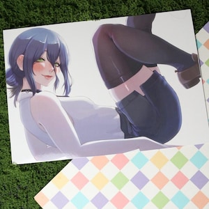 May include: A print featuring an anime-style illustration of a person with blue hair and green eyes, wearing a white top, dark shorts, and black tights. The person is lying down, with a playful expression. The print is on a white background, with a colorful patterned border.