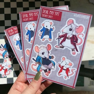May include: Three sticker sheets featuring cartoon rats dressed as characters from the video game Devil May Cry. The sticker sheets are labeled "Devil May Rat Sticker Sheet".