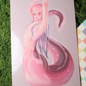 May include: A print featuring a nude figure with pink hair and a pink and purple tail. The figure's arms are raised above their head. The artwork has a soft, illustrative style with a light pink background.