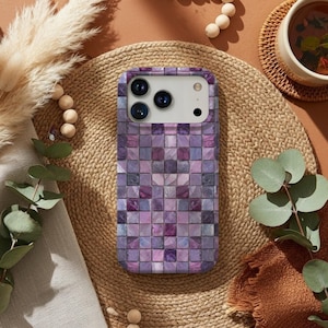 May include: A smartphone case featuring a mosaic tile pattern in shades of purple, lavender, and grey. The case is rectangular and designed to fit a smartphone, with camera and button cutouts. It rests on a woven mat.