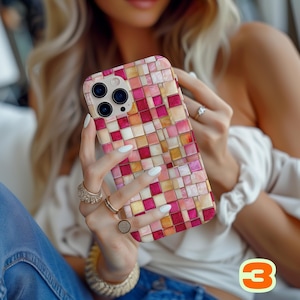 May include: A smartphone case with a mosaic tile design in shades of pink, red, and gold. The case has a square pattern and a camera cutout. The phone case is held by a person.