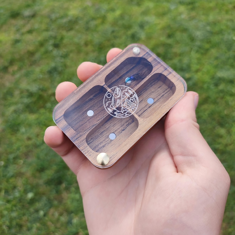 Puede incluir: Una caja de madera con cuatro compartimentos, cada uno con una tapa de acr&iacute;lico transparente. La caja tiene un dise&ntilde;o de un pez y monta&ntilde;as en la parte delantera.