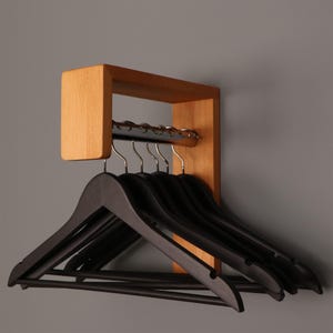 May include: A wall-mounted light wood rack featuring a horizontal metal bar with several silver hooks. Five black wooden clothes hangers are suspended from the hooks, each featuring a horizontal bar across the bottom for hanging garments.