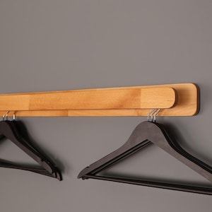 May include: A wooden wall-mounted hanger with two sets of black hangers. The hanger is made of light wood and has a simple design.