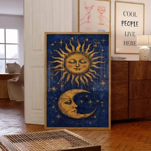May include: A rectangular framed wall art print featuring a golden sun with a human face and a golden crescent moon with a human face set against a deep blue starry night sky. The sun is positioned above the moon, both surrounded by golden stars.
