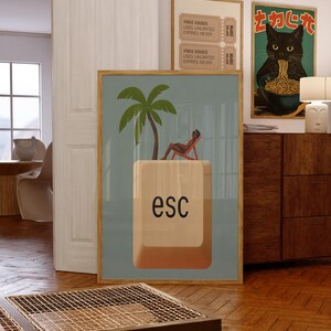 Framed whimsical poster featuring a person lounging under a palm tree on a giant “esc” keyboard key, styled in a cozy interior with playful and modern artwork.