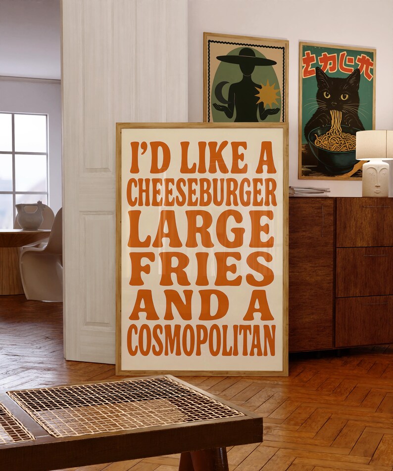 Retro kitchen wall art featuring bold orange typography that reads “I’d like a cheeseburger, large fries, and a cosmopolitan,” styled in a cozy mid-century space with wood and eclectic decor