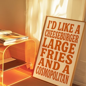 Cheeseburger and cosmopolitan poster glowing in golden hour light beside a translucent orange table and soft curtains.
