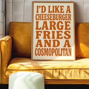 Funny orange quote poster leaning on a yellow couch, styled in a modern interior with tiled wall and sunlight.