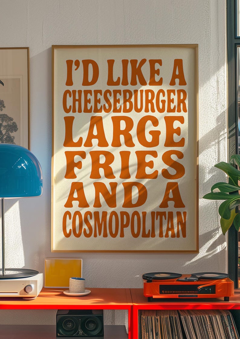 Bold orange typography print with cheeseburger and cosmopolitan quote styled in a retro living room with vinyl player and blue lamp.