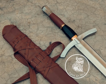 May include: A medieval-style sword with a silver blade and a brown leather-wrapped handle. The sword is next to a brown leather sheath with intricate stitching. The image also includes a logo that says "Zahid Art Work".
