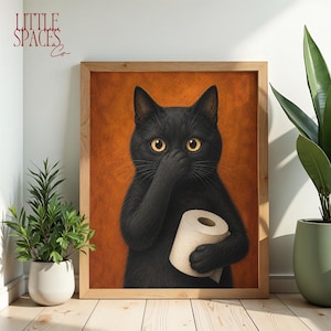 Può includere: Una stampa artistica incorniciata raffigurante un gatto nero con occhi gialli che tiene un rotolo di carta igienica e si copre il naso con una zampa. Lo sfondo è di colore arancione testurizzato. Il testo LITTLE SPACES Co è in alto a sinistra.