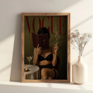 Peut inclure: Une impression d'art mural encadrée représentant une couverture de magazine intitulée VOGUE en lettres rouges. L'image montre une personne en lingerie noire tenant un livre rouge foncé avec une icône de verre à martini, fumant et assise à une table.