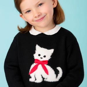 Peut inclure: Pull noir avec un motif de chat blanc et un nœud rouge. Le pull a un col blanc. La fille porte un bandeau bleu et une jupe rouge. Le fond est bleu clair.