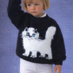 May include: A dark navy blue sweater with a white cat design. The cat has blue eyes and a fluffy tail. The sweater is worn with white pants. The background is a solid blue.