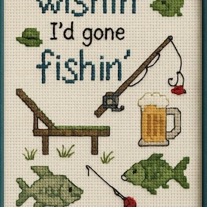 Puede incluir: Obra de arte de punto de cruz en un marco verde azulado con las palabras "Wishin' I'd gone fishin'" e ilustraciones temáticas de pesca. Incluye una caña de pescar, peces, una jarra de cerveza y una tumbona.