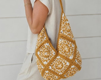 Pode incluir: Uma bolsa de ombro estilo hobo feita de quadrados de crochê nas cores amarelo mostarda e branco. A bolsa apresenta um padrão geométrico repetitivo inspirado em flores, com uma alça integrada e um formato flexível e sem estrutura.