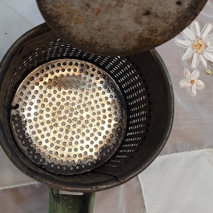 May include: A vintage green metal potato ricer with a removable lid and a perforated metal bowl. The ricer is used to mash potatoes and other vegetables.