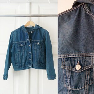 May include: A blue denim jacket with a hood. The jacket has a button closure and two pockets.