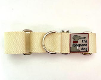 May include: A cream-colored dog collar with silver hardware and a patch that says "the longnose dog" in black text.