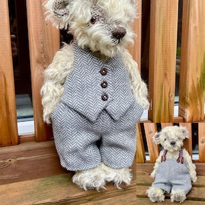 Op de afbeelding: Twee handgemaakte teddyberen. De grotere beer draagt een grijs visgraatvest en -broek met drie bruine knopen. De kleinere beer draagt een grijze overall met paarse en bruine bandjes. Beide beren hebben crèmekleurige vacht en bruine neuzen.