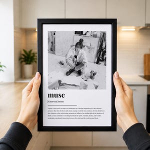 May include: A black framed wall art print featuring a black and white photograph of an artist in a studio above the dictionary-style definition of the word muse, including the noun vanessa and a descriptive paragraph about the nature of inspiration.