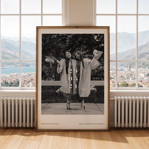 Puede incluir: Una fotografía en blanco y negro enmarcada de dos graduados con birretes y togas, celebrando. La foto incluye la fecha "20 05 21" y los lugares "Pennsylvania, USA" y "Williamsburg University". El marco es de color marrón cálido.