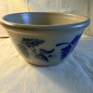 May include: A stoneware mixing bowl with a light beige exterior and a blue floral design. The bowl has a wide rim and a slightly flared shape. The blue leaf pattern is repeated around the bowl's exterior.