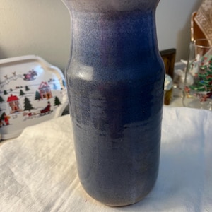 May include: A tall, handcrafted ceramic vase with a gradient of blue hues. The vase has a wide opening and a cylindrical body. The colors transition from a light blue at the top to a deep blue at the base. The vase is likely used for decorative purposes.