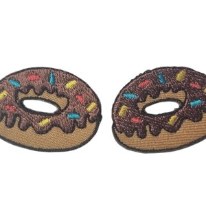 Peut inclure: Deux écussons brodés en forme de donut avec glaçage au chocolat et des vermicelles colorés. Les écussons ont une base marron et un bord marron clair, parfaits pour les vêtements ou accessoires.
