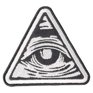 Puede incluir: Parche bordado con un triángulo negro y borde blanco. En el interior, un diseño de ojo blanco, con iris y líneas detalladas. El parche es probablemente para ropa o accesorios.