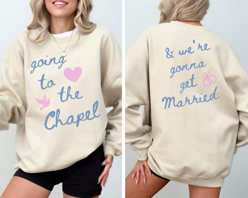 May include: Beige sweatshirt with the text "going to the Chapel" in blue script, a pink heart, and a dove graphic. The back of the sweatshirt says "& we're gonna get Married" in blue script with pink wedding rings.