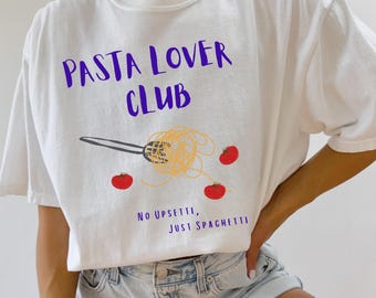 May include: White t-shirt with the text "PASTA LOVER CLUB" in purple. Below the text is a graphic of spaghetti and a fork, with three red tomatoes. The phrase "NO UPSETTI, JUST SPAGHETTI" is printed below the graphic.