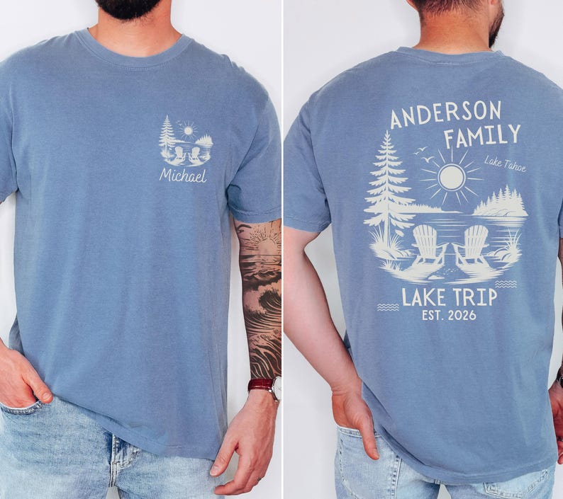 May include: A blue t-shirt featuring a small graphic on the front left chest with a sun, trees, and the name Michael. The back displays a large graphic of two chairs by a lake, trees, a sun, and the text Anderson Family Lake Trip Est. 2026.