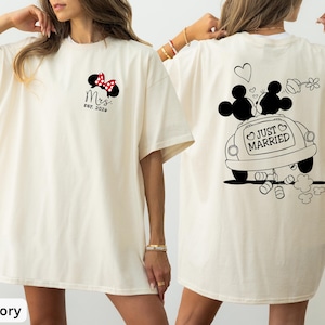 May include: Ivory t-shirt with a Minnie Mouse design and red bow, plus "Mrs. EST. 2020" on the front. The back shows a black and white graphic of Mickey and Minnie Mouse in a car with "Just Married" text.