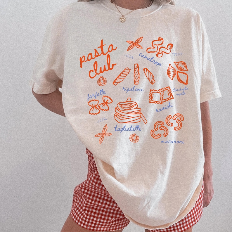 Pu&ograve; includere: T-shirt color crema con la scritta "pasta club" in arancione. La maglietta presenta illustrazioni arancioni di varie forme di pasta, tra cui farfalle, rigatoni e ravioli. Il design &egrave; un omaggio giocoso alla cucina italiana.