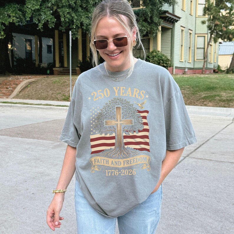 May include: A gray t-shirt with a graphic design commemorating 250 years. The design includes a cross, tree, American flag, and the text "Faith and Freedom 1776-2026". The shirt is a relaxed fit.