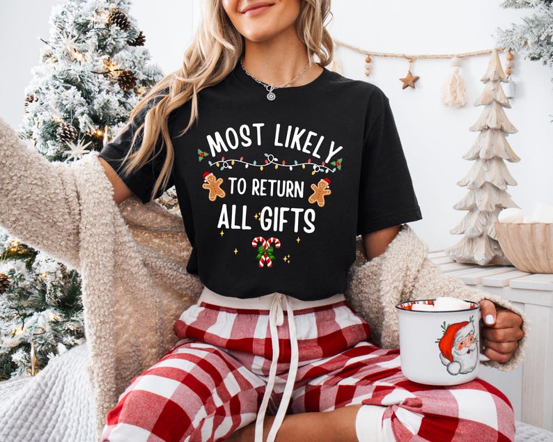 May include: A black short-sleeved t-shirt featuring the white text MOST LIKELY TO RETURN ALL GIFTS, decorated with colorful string lights, two gingerbread cookies, and two candy canes with green holly leaves and red berries.