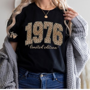 以下が含まれることがあります： 黒いTシャツ。ヒョウ柄の「1976」の文字。その下に「limited edition」の文字。左袖には「chapter 50」の文字とハートのグラフィック。