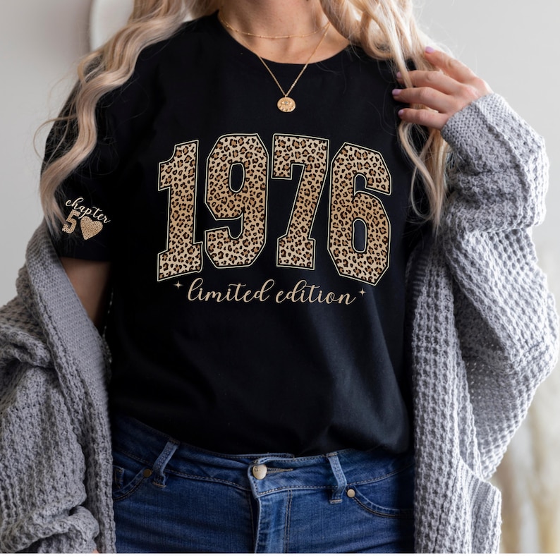 以下が含まれることがあります： 黒いTシャツ。ヒョウ柄の「1976」の文字。その下に「limited edition」の文字。左袖には「chapter 50」の文字とハートのグラフィック。