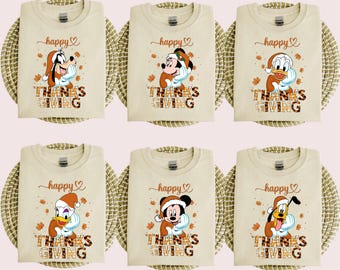 May include: Beige t-shirts with Thanksgiving-themed graphics featuring cartoon characters. Each shirt displays "happy" above and "THANKS GIVING" below, with fall leaves. Characters include Goofy, Mickey Mouse, Donald Duck, and Pluto.