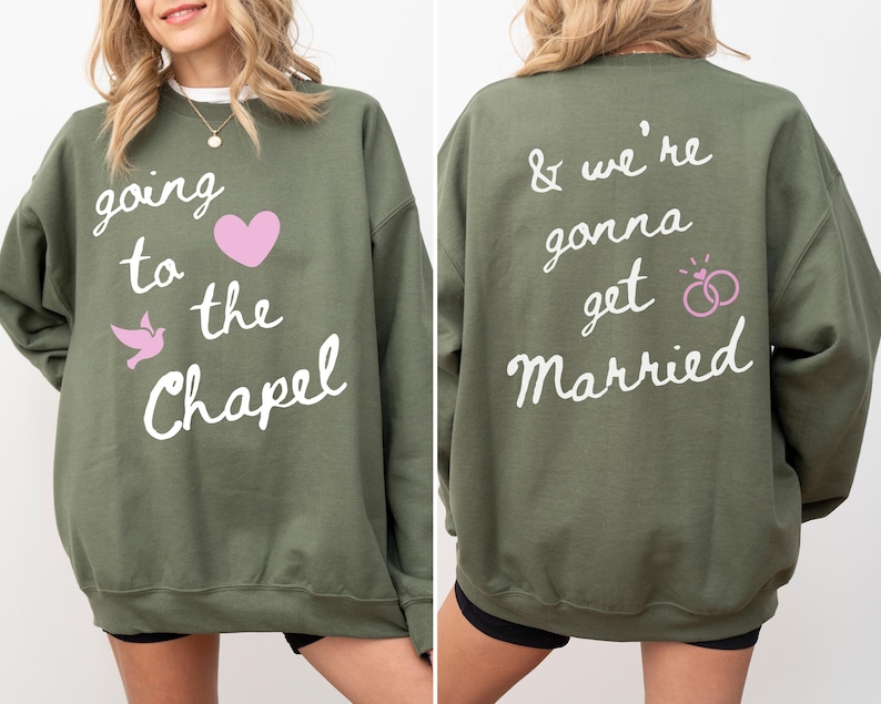 May include: Olive green sweatshirt with the text "going to the Chapel" and a pink heart and dove graphic on the front. The back of the sweatshirt says "& we're gonna get Married" with a pink rings graphic. A casual wedding-themed top.