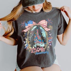 K&ouml;nnte beinhalten: Dunkelgraues T-Shirt mit einer farbenfrohen Grafik eines Schlosses in einem goldenen Oval, verziert mit einer rot-wei&szlig;-blauen Schleife. Die Grafik enth&auml;lt Feuerwerk und den Text "250th Anniversary".