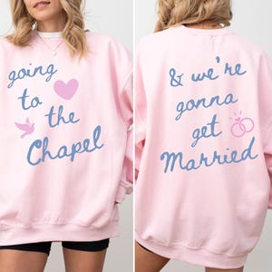 May include: A light pink sweatshirt with the text "going to the Chapel" and "& we're gonna get Married" in blue script. The front features a pink heart and a dove graphic. The back has a ring graphic.