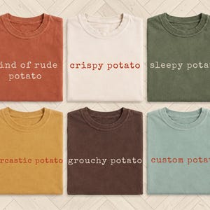 Op de afbeelding: Zes T-shirts met ronde hals in verschillende kleuren, waaronder roest, crème, olijf, mosterd, donkerbruin en saliegroen. Elk T-shirt heeft tekst op de voorkant gedrukt: kind of rude potato, crispy potato, sleepy potato, sarcastic potato, grouchy potato, custom potato.