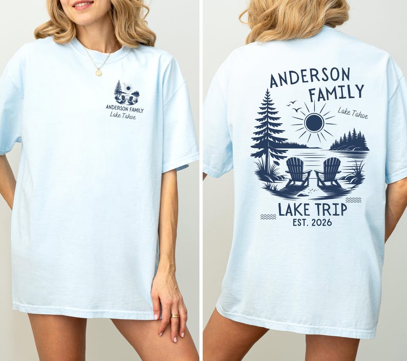 May include: A light blue short-sleeved t-shirt featuring a dark blue graphic print. The front displays a small lake scene with two chairs and the text "Anderson Family Lake Tahoe." The back features a larger version of the same graphic.