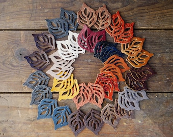 Peut inclure: Une collection de 20 formes de feuilles en cuir de différentes couleurs, dont le brun, le beige, le rouge, l'orange, le jaune et le bleu. Les feuilles sont disposées en cercle sur une surface en bois.