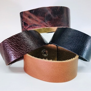 May include: Four leather bracelets in different colors and textures. The bracelets are stacked on top of each other. The top bracelet is a dark brown with a marbled pattern. The second bracelet is a dark brown with a smooth texture. The third bracelet is a black leather bracelet with a smooth texture. The bottom bracelet is a light brown leather bracelet with a smooth texture.
